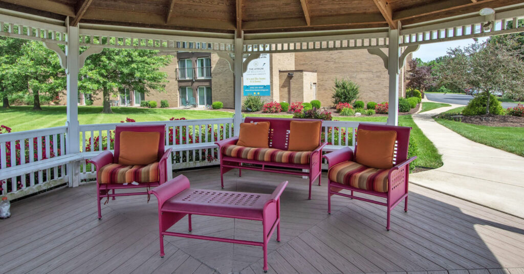 A gazebo with a pink couch and two pink sofa chairs with orange throw pillows on them and a pink coffee table in front of them at Atrium of Belleville.