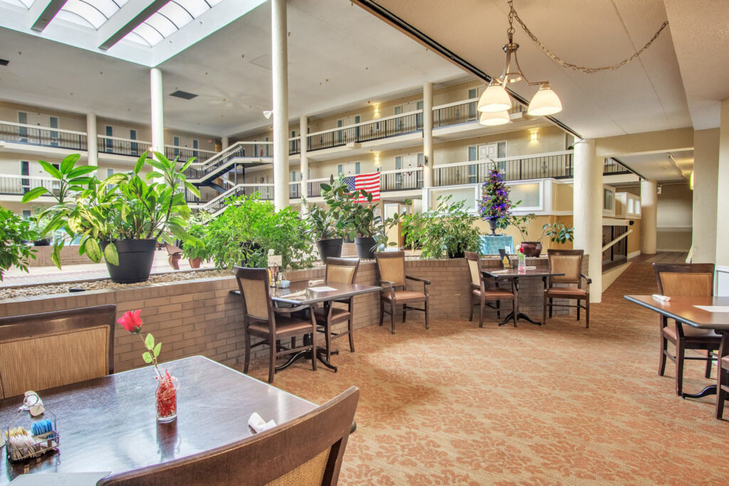 A dining area with brown tables and chairs, and a single pink flower sitting in a little vase on each table at The Atrium of Belleville.