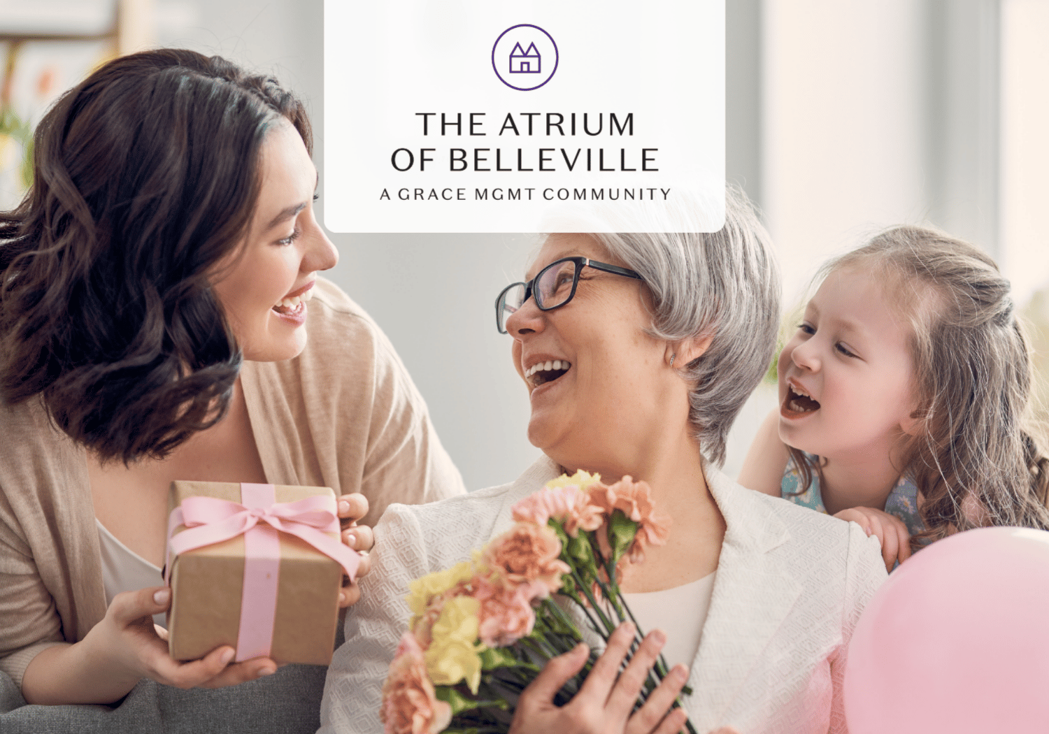 Three generations share a joyful moment: a younger woman hands a gift to an elderly woman holding flowers, with a smiling child nearby.