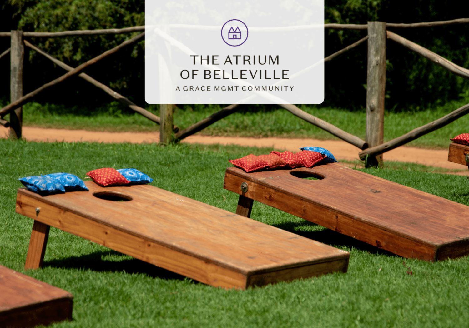 Outdoor lawn with two wooden cornhole boards and colorful pillows, likely part of a community event at The Atrium of Belleville.